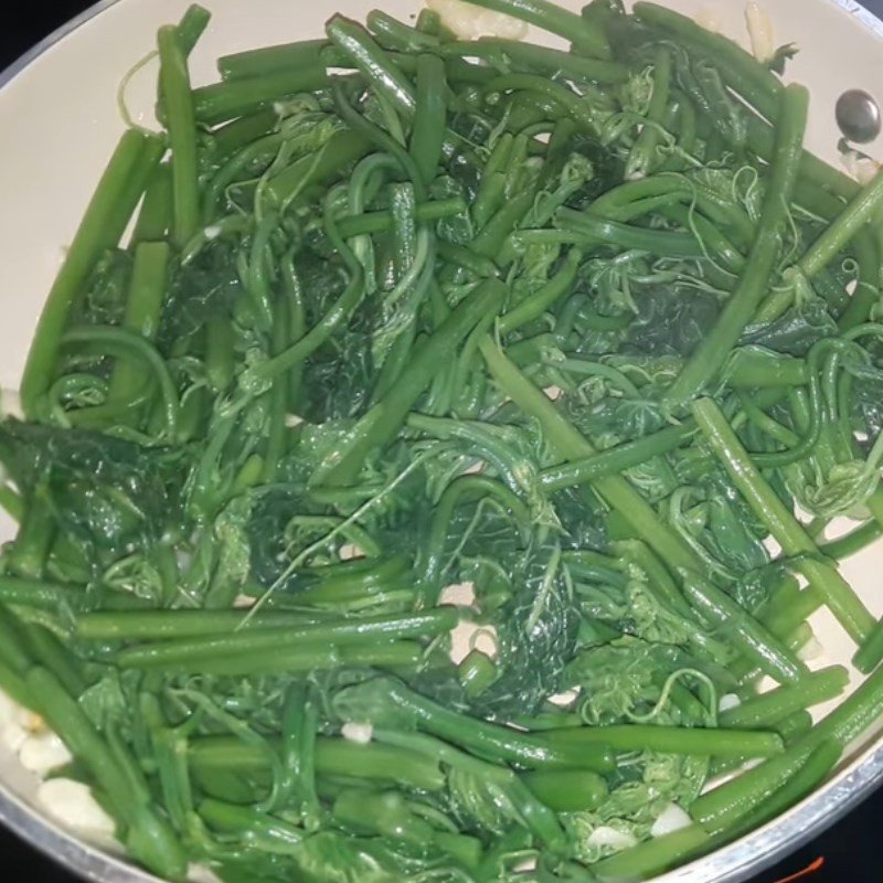 Chảo ngọn su su xào tỏi đã chín, rau chuyển màu xanh sẫm, sẵn sàng để bày ra đĩa
