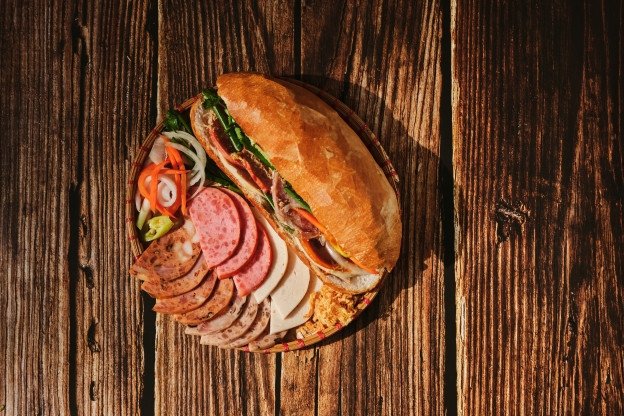 Một ổ bánh mì Huỳnh Hoa thơm ngon, vàng giòn được kẹp đầy đủ nhân và rau củ tươi, thể hiện độ lớn và hấp dẫn của món ăn