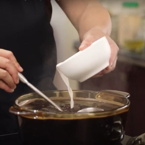 Nồi chè đỗ đen đang được ninh trên bếp, hạt đỗ vẫn còn nguyên vẹn trong nước.